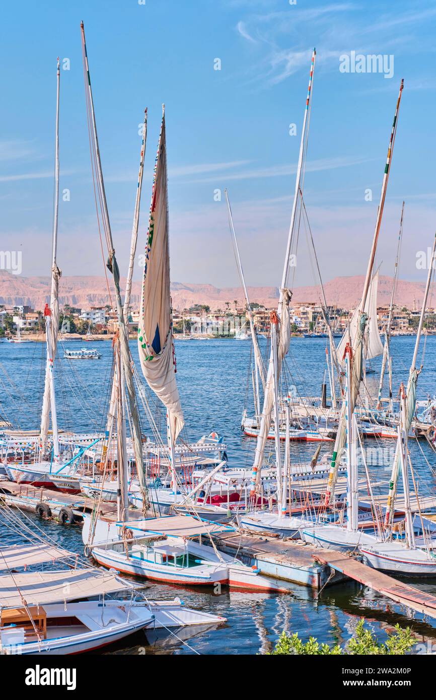 Louxor, Égypte - décembre 26 2023 : feries à moteur traditionnelles et bateaux à voile Felucca amarrés le long du Nil Banque D'Images