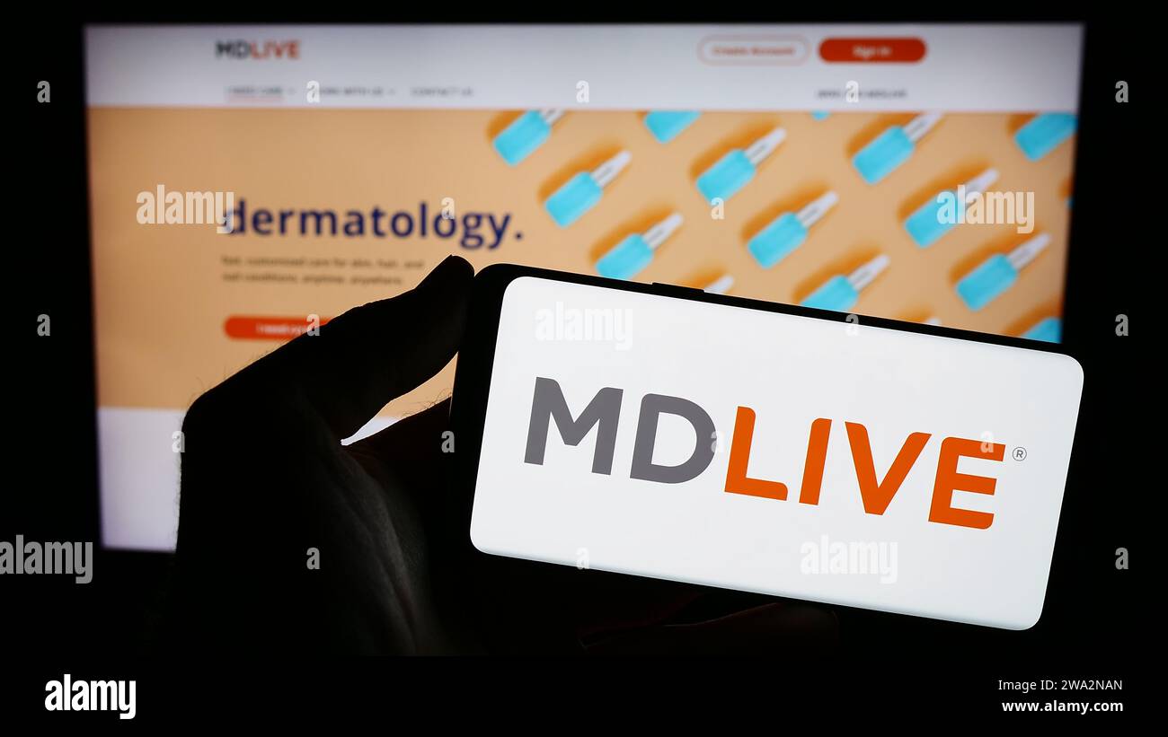 Personne détenant le smartphone avec le logo de la société de services de santé virtuelle américaine MDLIVE en face du site Web. Concentrez-vous sur l'affichage du téléphone. Banque D'Images