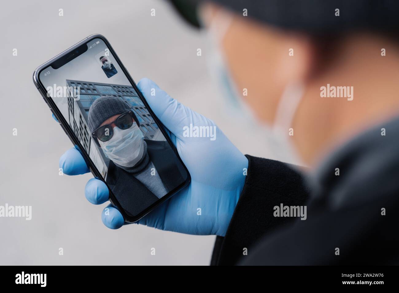 Personne portant des gants et un masque tenant un téléphone pendant un appel vidéo, reflétant la nouvelle norme de communication en période de pandémie Banque D'Images