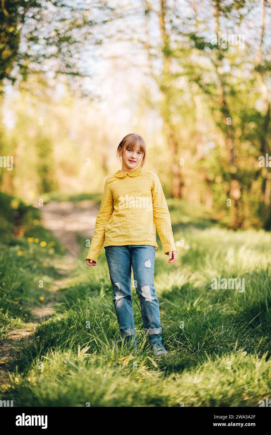 Portrait en plein air de jolie petite fille dans la forêt de printemps, portant un chemisier vert et un Jean Banque D'Images