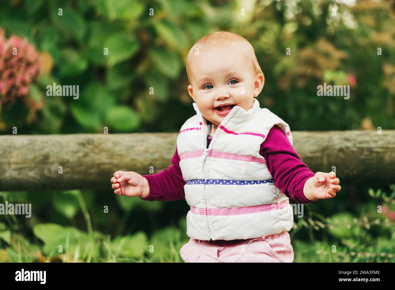 Portrait en plein air d'une adorable petite fille de 9-12 mois jouant dans le parc, portant un chauffe-corps blanc Banque D'Images