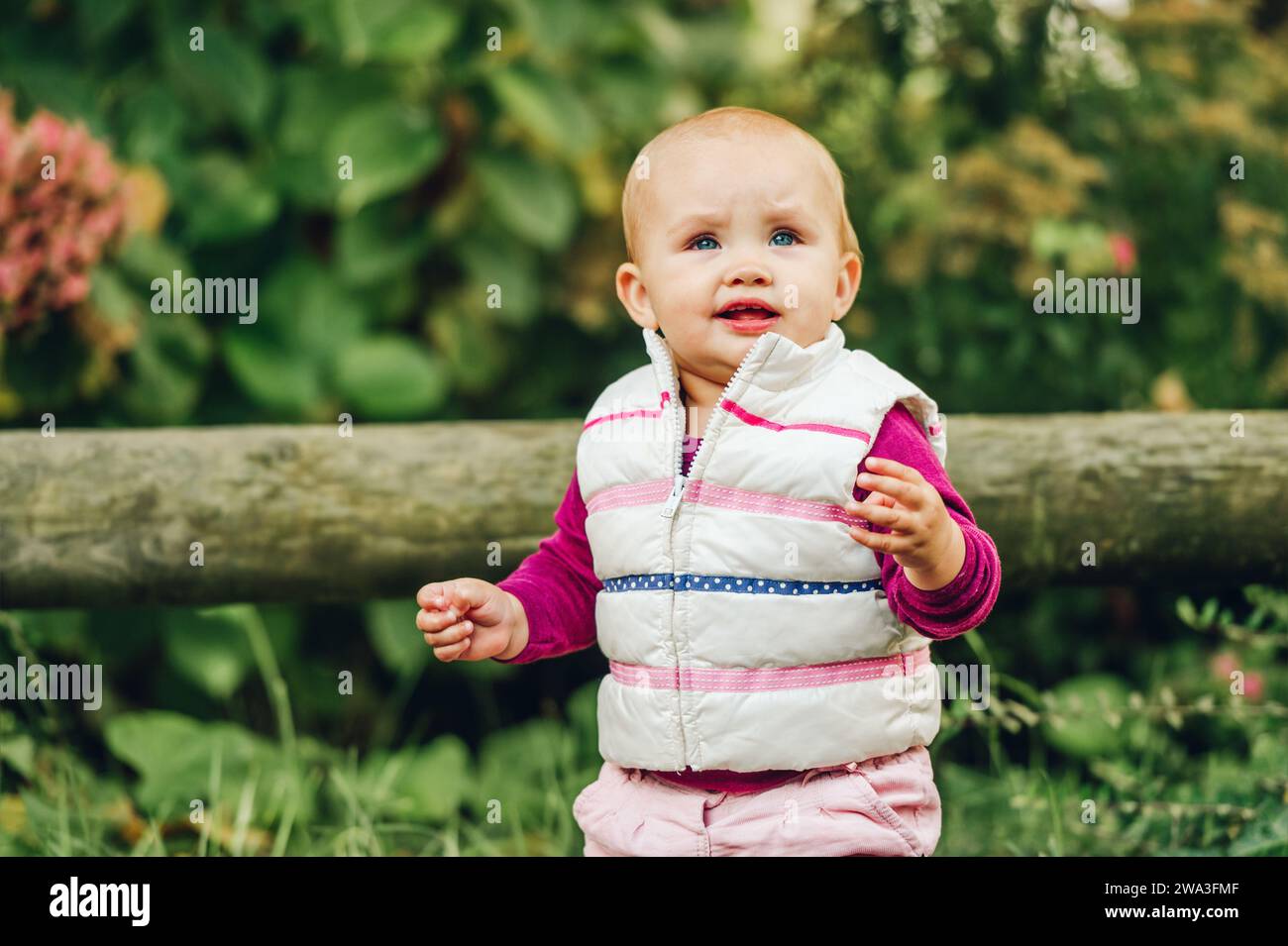 Portrait en plein air d'une adorable petite fille de 9-12 mois jouant dans le parc, portant un chauffe-corps blanc Banque D'Images