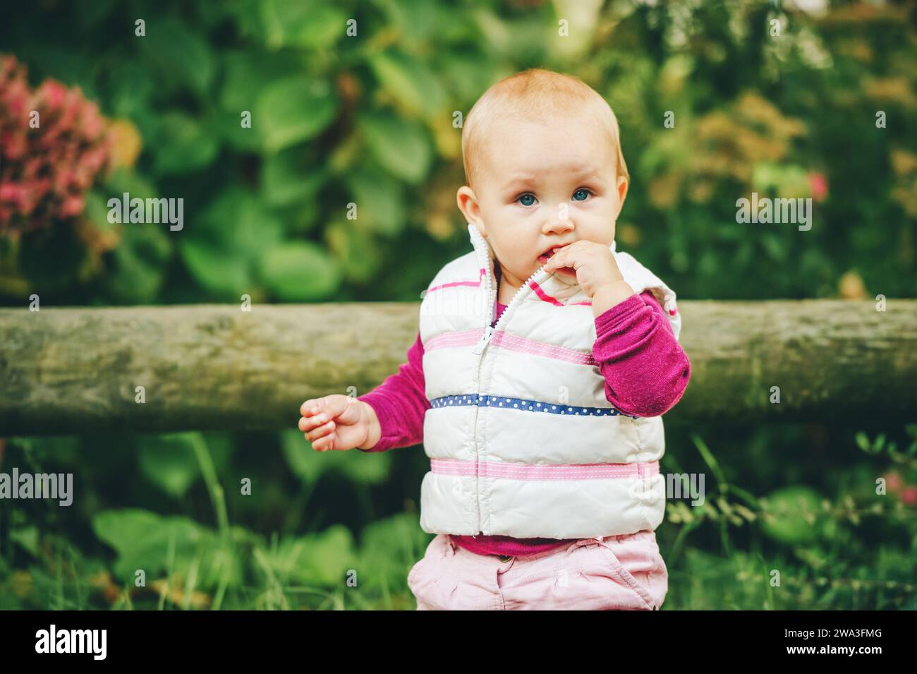 Portrait en plein air d'une adorable petite fille de 9-12 mois jouant dans le parc, portant un chauffe-corps blanc Banque D'Images