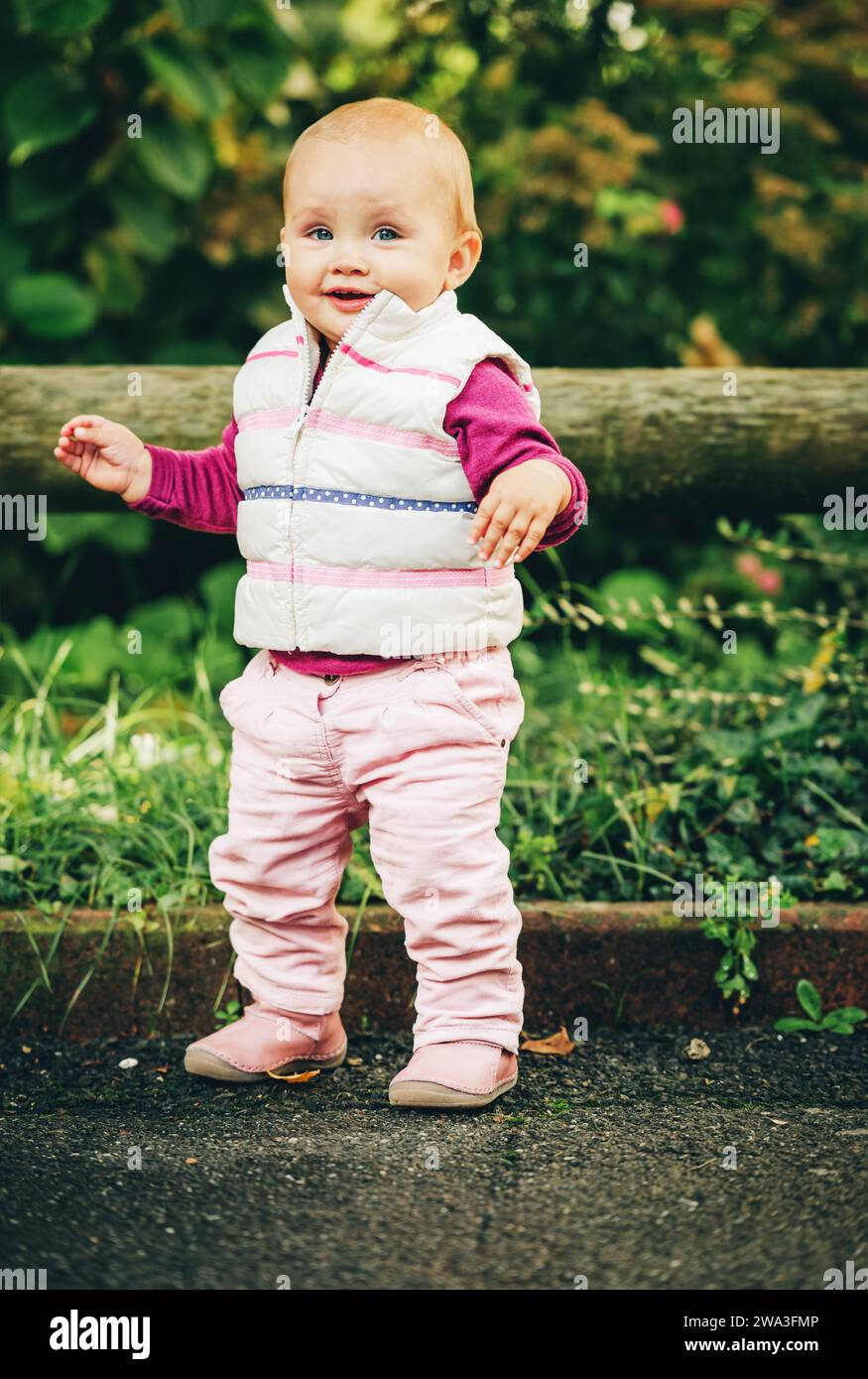 Portrait en plein air d'une adorable petite fille de 9-12 mois jouant dans le parc, portant un chauffe-corps blanc Banque D'Images