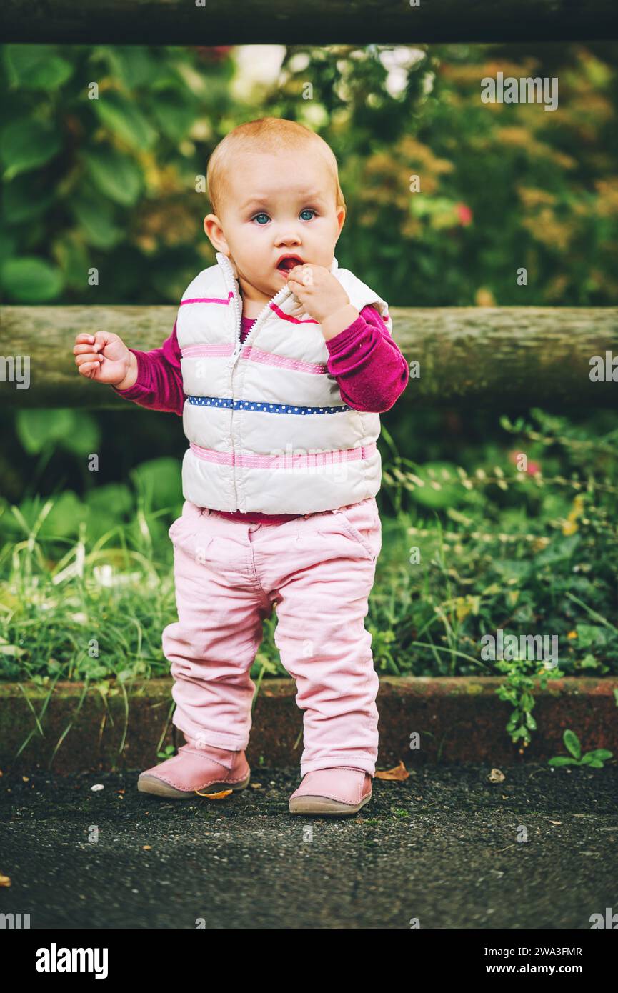 Portrait en plein air d'une adorable petite fille de 9-12 mois jouant dans le parc, portant un chauffe-corps blanc Banque D'Images