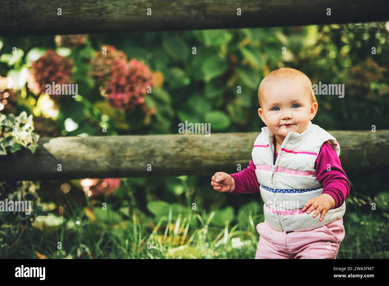 Portrait en plein air d'une adorable petite fille de 9-12 mois jouant dans le parc, portant un chauffe-corps blanc Banque D'Images