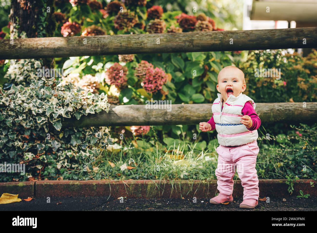 Portrait en plein air d'une adorable petite fille de 9-12 mois jouant dans le parc, portant un chauffe-corps blanc Banque D'Images