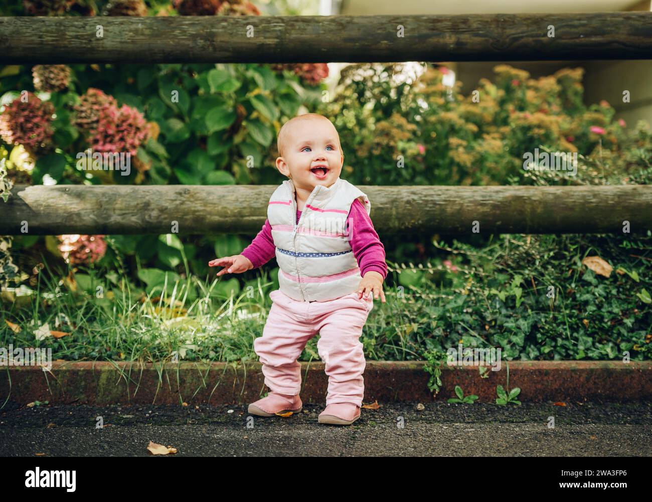 Portrait en plein air d'une adorable petite fille de 9-12 mois jouant dans le parc, portant un chauffe-corps blanc Banque D'Images