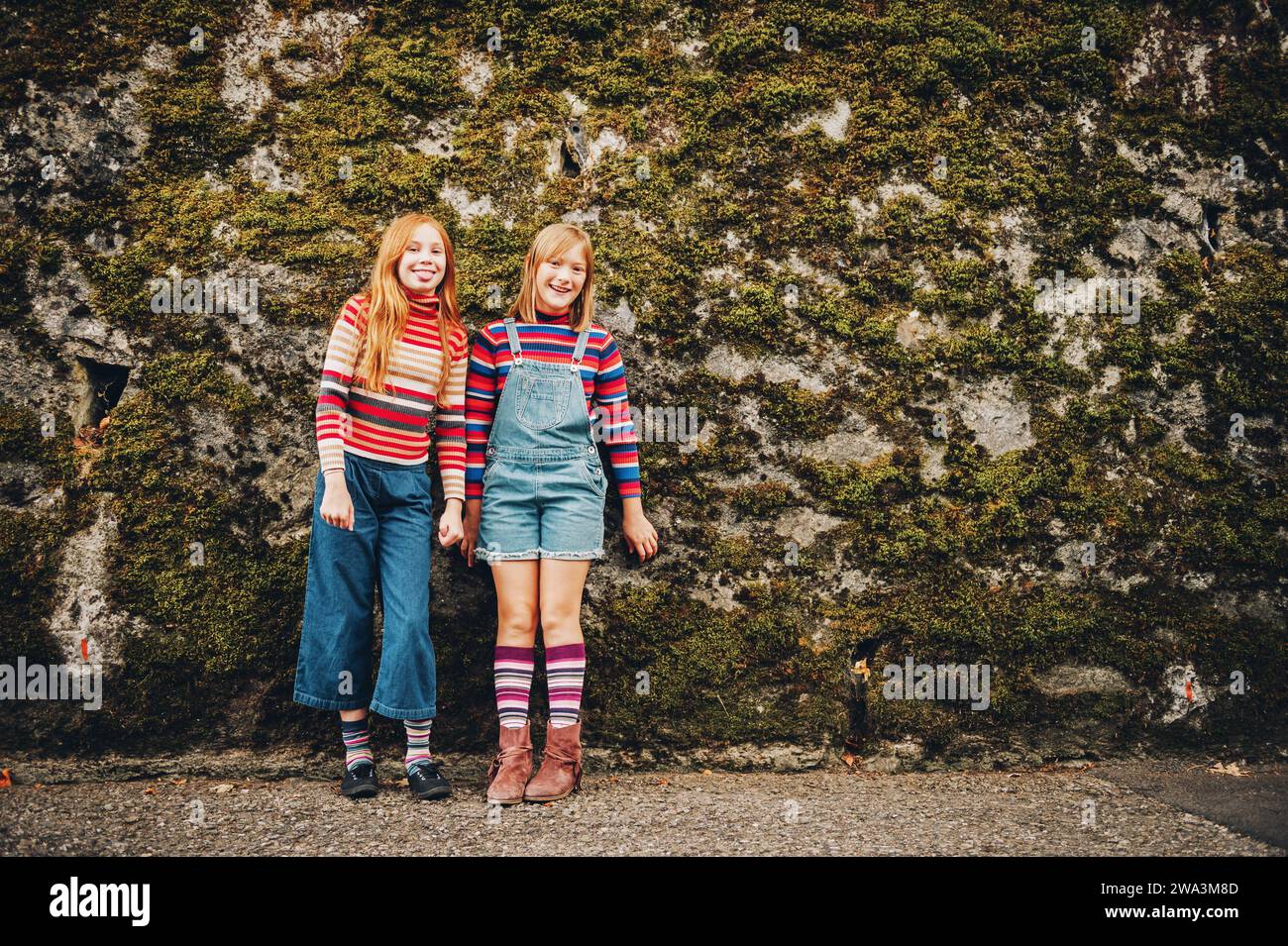 Portrait en plein air de deux drôles de préadolescents portant des shorts en denim, des pulls à col roulé rayé et des chaussettes longues, posant contre le mur de mousse, mode pour tee-shirt Banque D'Images