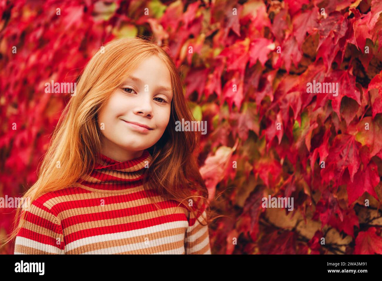 Portrait rapproché en plein air d'adorable fille préadolescente de 10 ans, appuyé sur le mur de lierre rouge. Enfant avec de longs cheveux roux profitant d'une belle journée d'automne Banque D'Images