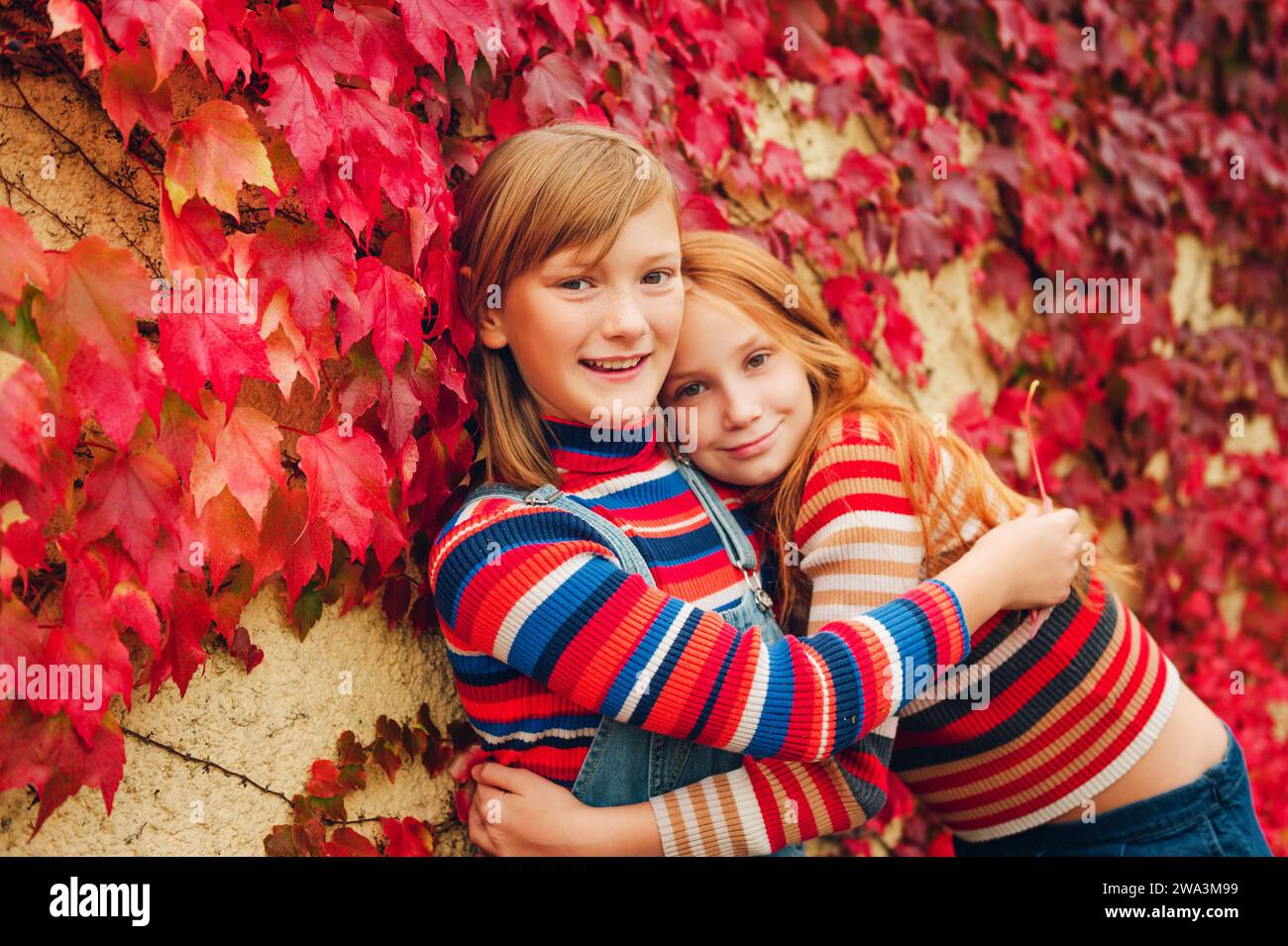 Portrait d'automne de deux filles drôles jouant ensemble à l'extérieur, posant contre le mur de lierre rouge. Mode d'automne pour les adolescents Banque D'Images