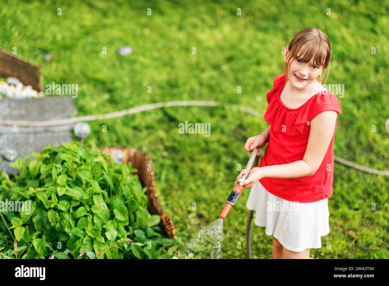 Kid girl arrosage des plantes dans le petit jardin, vue de dessus Banque D'Images