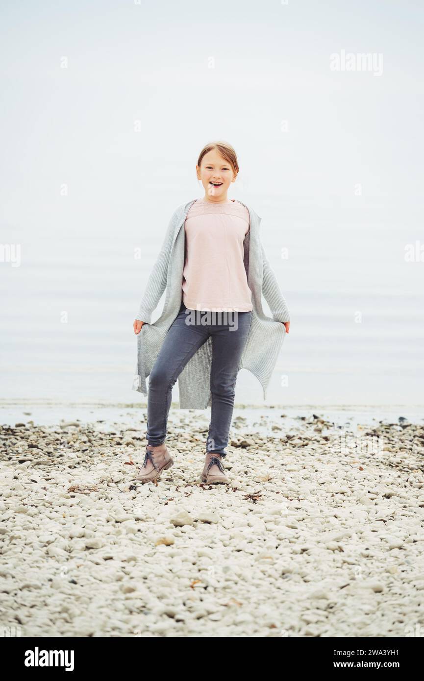 Adorable petite fille de 8-9 ans jouant au bord du lac, portant un pantalon gris et un long cardigan Banque D'Images