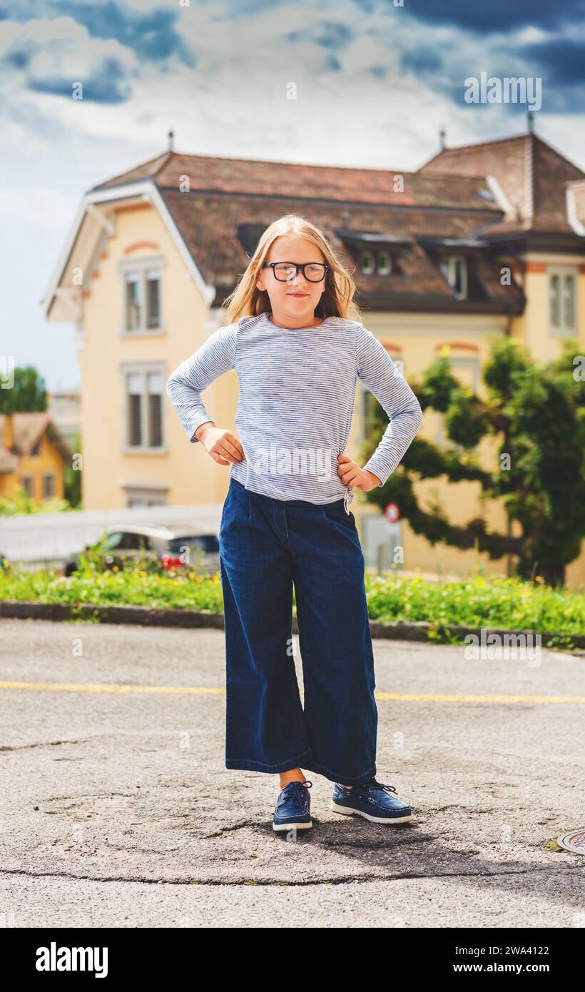 Portrait drôle en plein air d'une jolie petite fille de 9-10 ans portant un haut bleu, des culottes en denim et des lunettes Banque D'Images