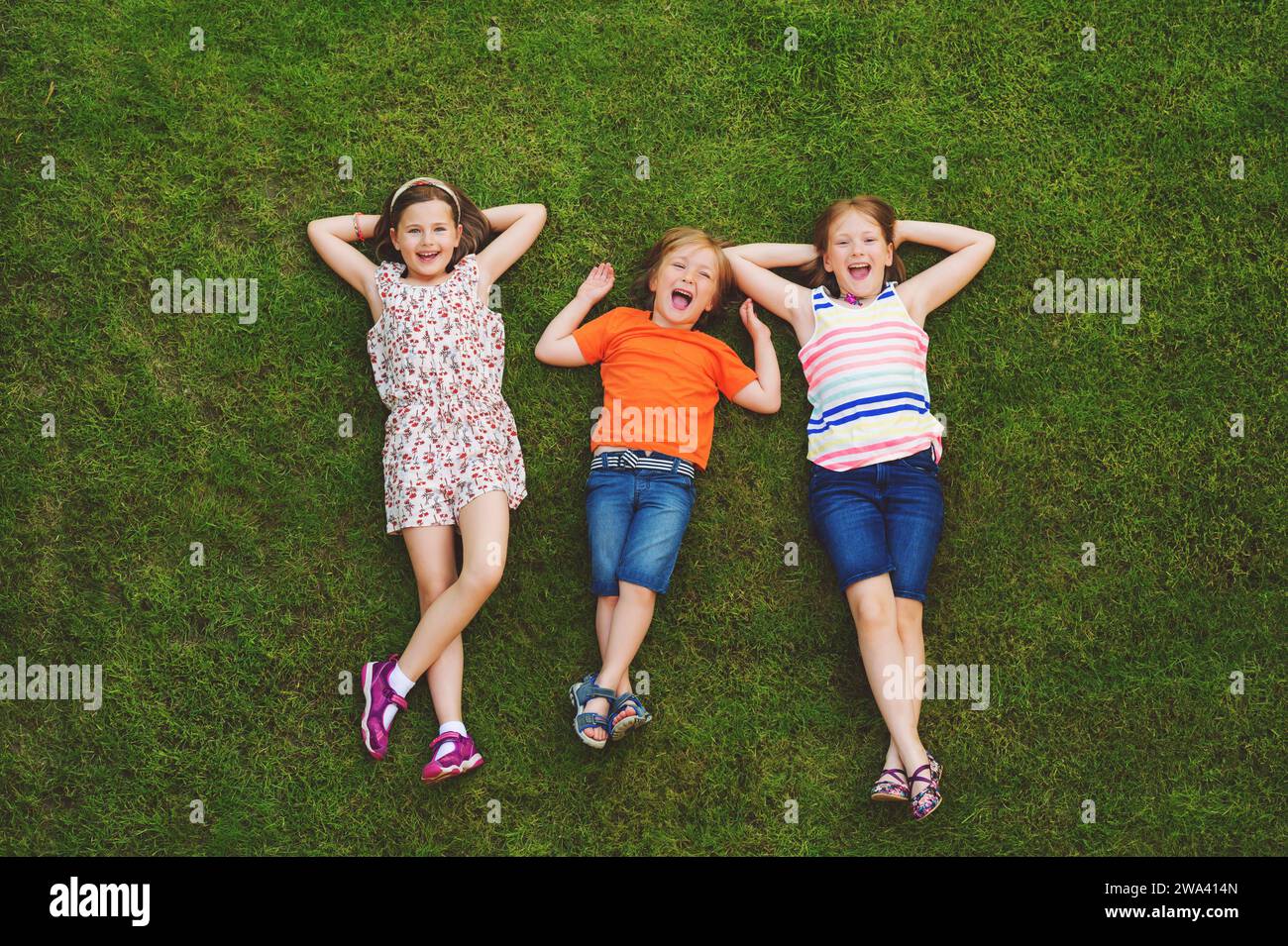 Enfants heureux s'amusant à l'extérieur. Enfants jouant dans le parc d'été. Petit garçon et deux filles allongées sur de l'herbe verte fraîche Banque D'Images