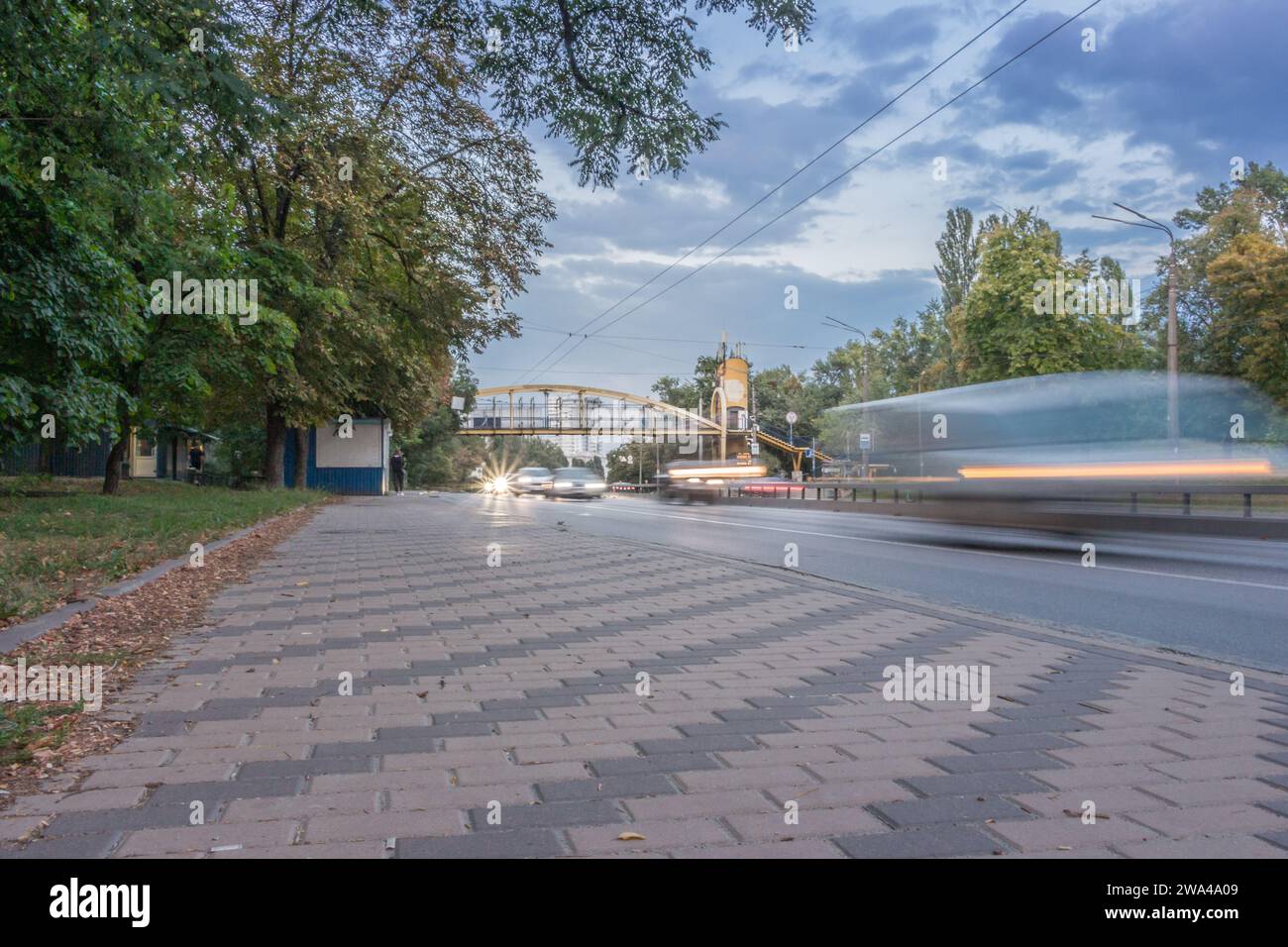 Circulation sur l'autoroute en mouvement. Trafic dans la ville de soirée d'été. Voitures en mouvement avec des lumières le long du trottoir. Scène urbaine avec transport. Banque D'Images