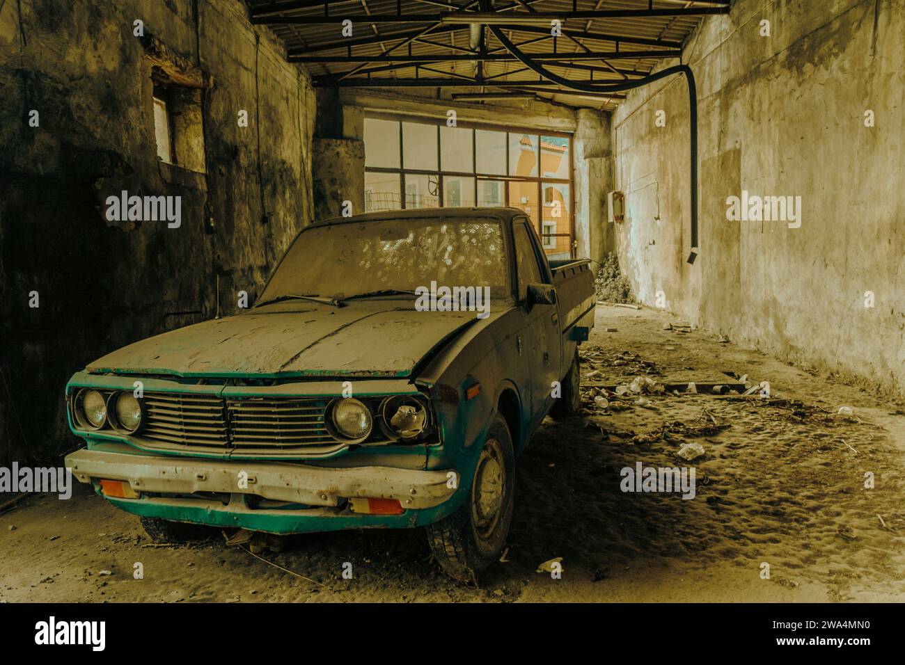 Voiture ancienne abandonnée couverte de poussière à l'intérieur d'un garage en décomposition avec lumière naturelle. Banque D'Images