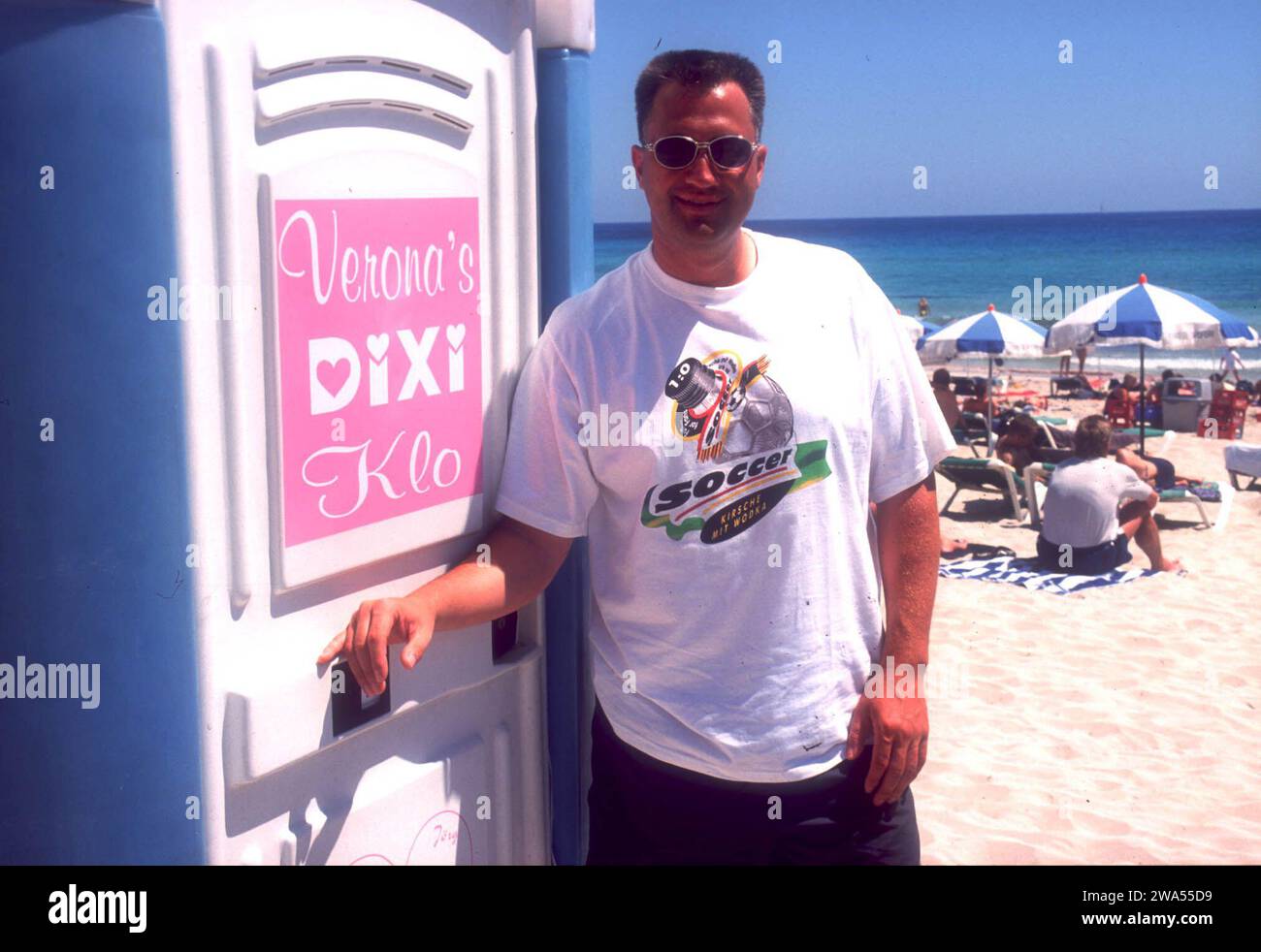 Männer posieren vor und mit Verona's DIXI Klo vom Auftritt von Verona Feldbusch BEI 'Big Brother' am Strand auf Mallorca, Espagne 2000. Banque D'Images