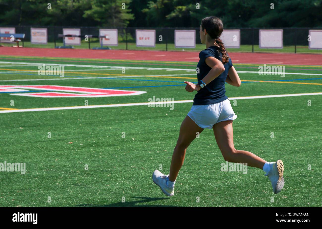 Vue arrière d'une femme courant à travers un champ par une journée ensoleillée. Banque D'Images
