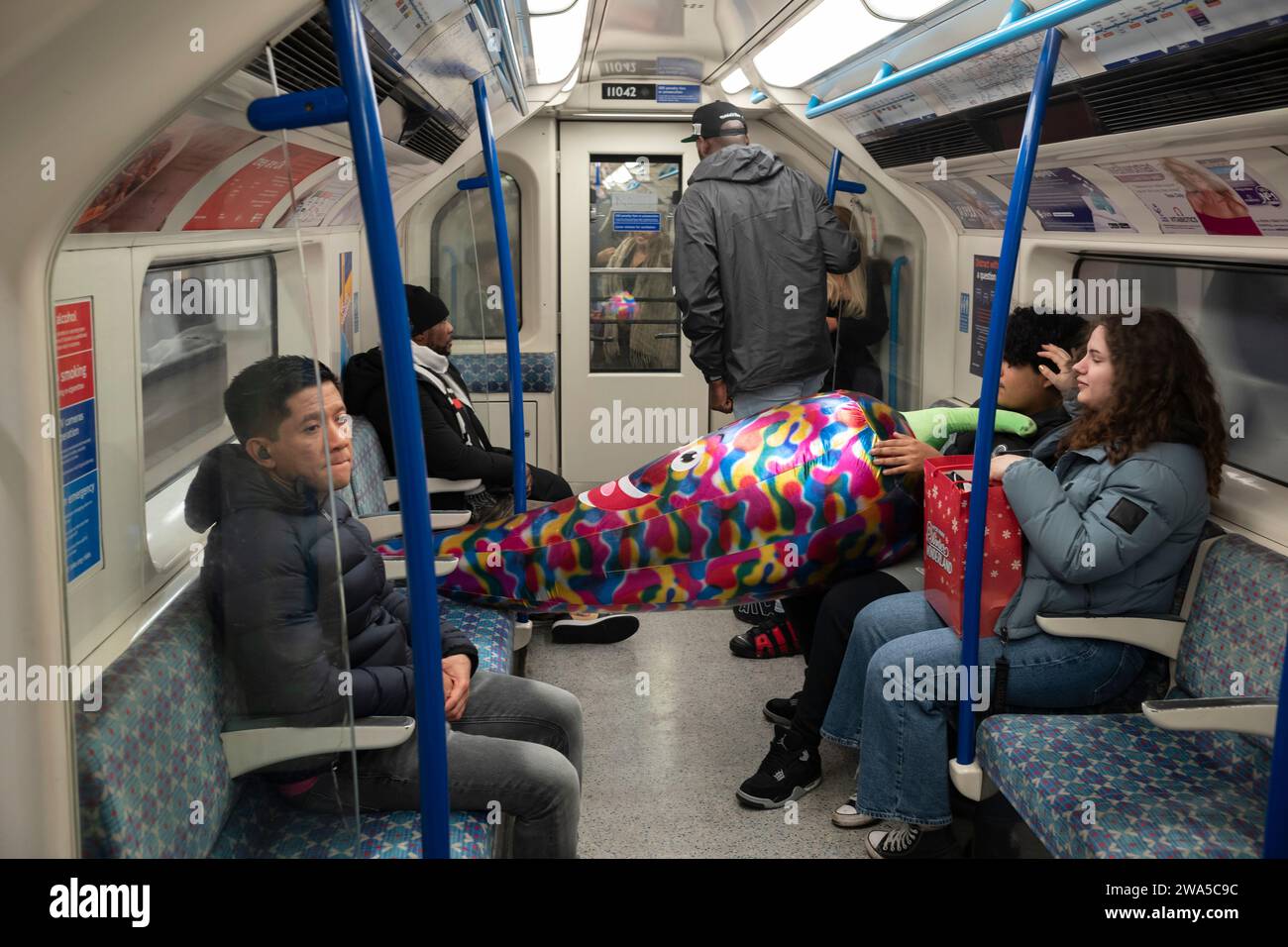 Les gens voyagent sur le métro de Londres transportant un grand jouet gonflable, Londres, Angleterre, Royaume-Uni. Banque D'Images
