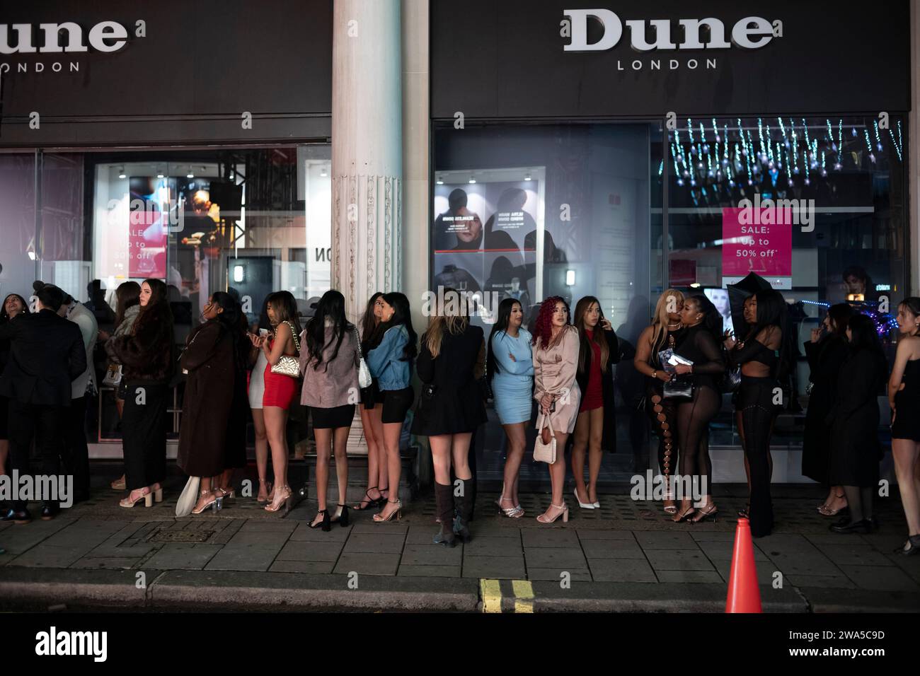 Les jeunes femmes font la queue devant une boîte de nuit lors d'une soirée du nouvel an humide en mottes dans le quartier du West End de la capitale, Londres, Angleterre, Royaume-Uni. Banque D'Images