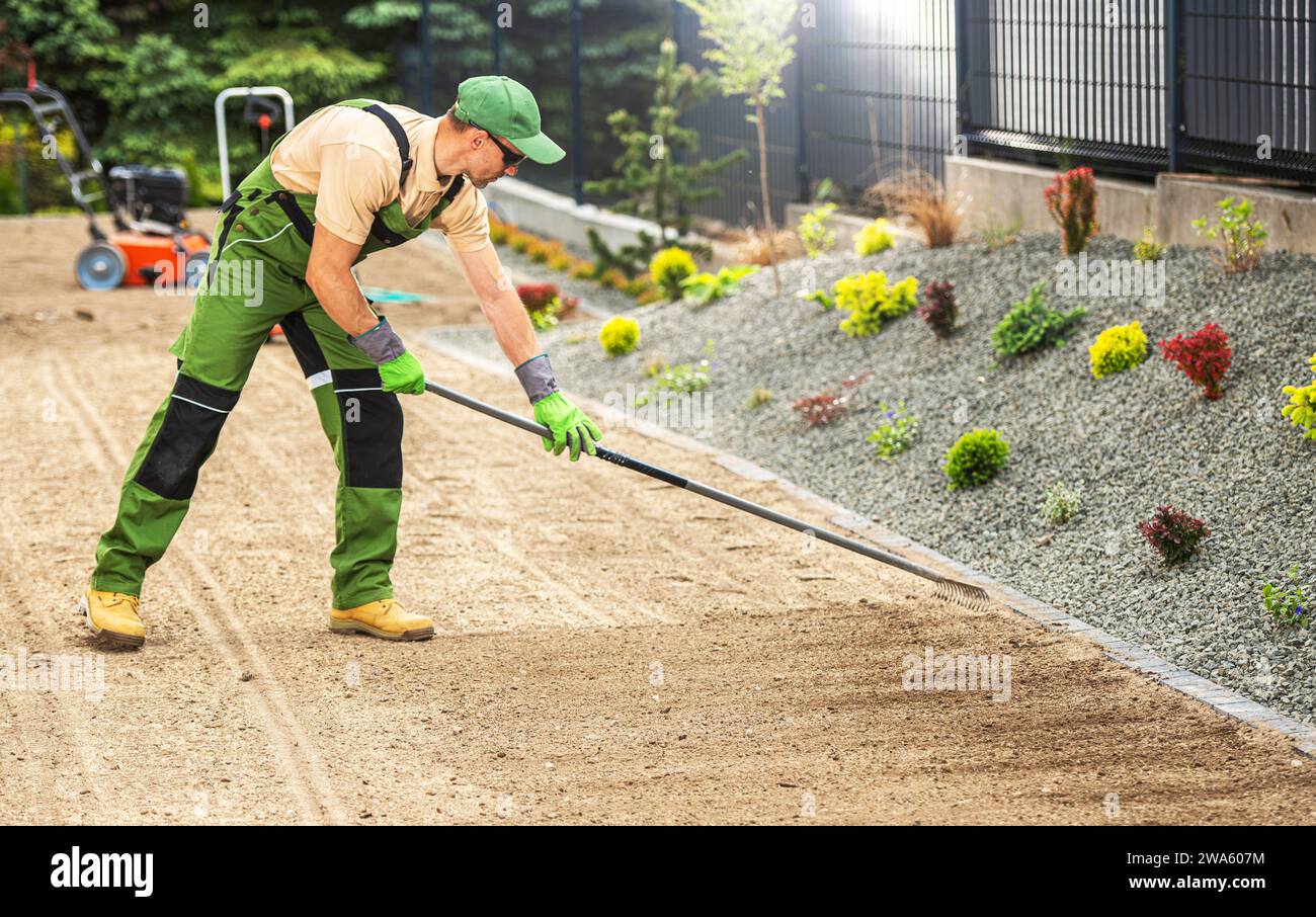 Caucasian Gardener dans ses années 40 préparer le sol d'arrière-cour résidentiel pour un ensemencement d'herbe. Râtelage du sol. Banque D'Images