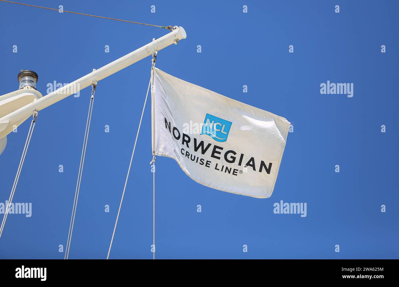 Norwegian Cruise Line logo flag (NCL), le drapeau de la compagnie de croisières basée à Miami vole sur un mât de navire de croisière avec feu de navigation, fond de ciel bleu Banque D'Images
