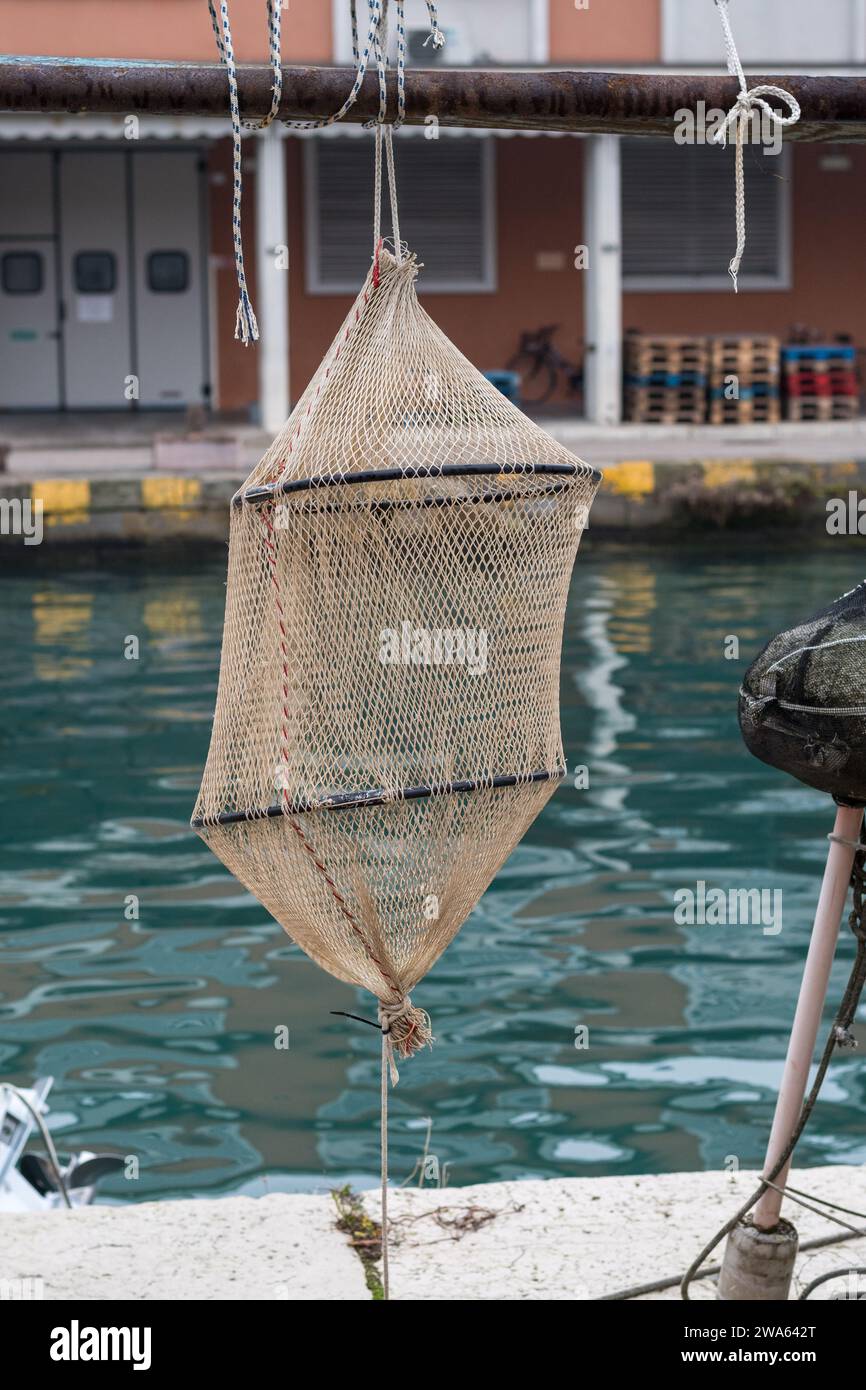 Articles pour set de pêche trouvés sur le port de Grado. Keepnet typique qui est descendu dans l'eau et suspendu à une certaine profondeur. Réaliste. Banque D'Images