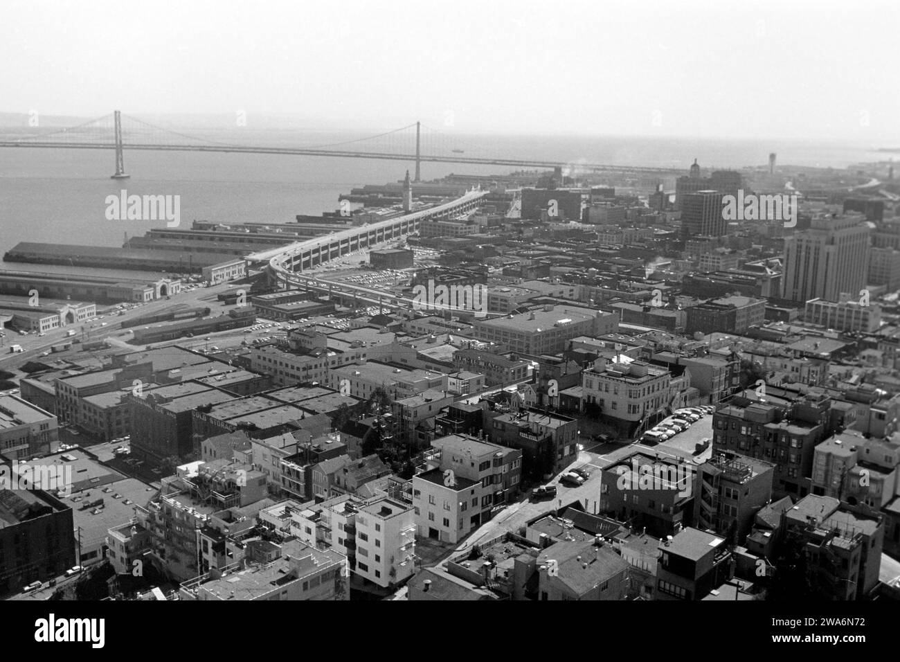 Blick über San Francisco mit der Oakland Bay Bridge, einigen Molen im Hafengebiet sowie dem Embarcadero Freeway, abgerissen 1991, vom Coit Aussichtsturm auf dem Telegraph Hill aus, 1962. Vue sur San Francisco avec le Oakland Bay Bridge, quelques jetées dans la zone portuaire et l'Embarcadero Freeway, démolie en 1991, depuis la tour d'observation de Coit sur Telegraph Hill, 1962. Banque D'Images