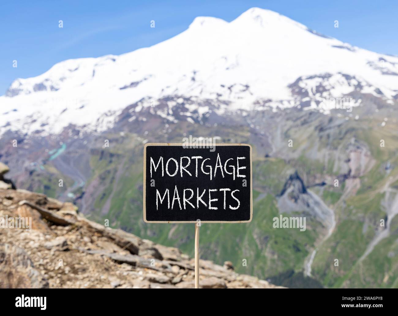 Symbole du marché hypothécaire. Mots concept marchés hypothécaires sur beau tableau noir de craie. Belle montagne Elbrus fond de ciel bleu. M Banque D'Images