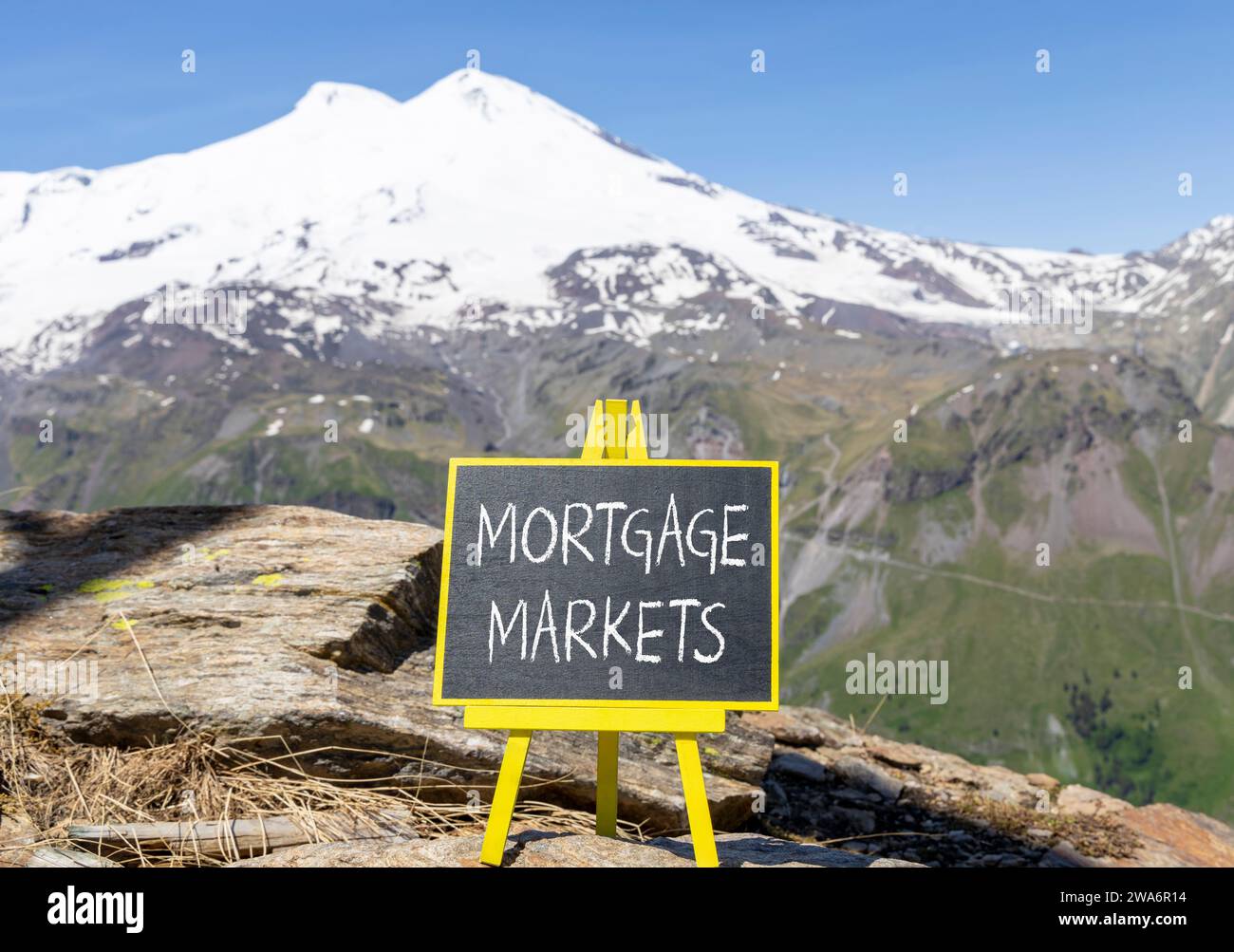 Symbole du marché hypothécaire. Mots concept marchés hypothécaires sur beau tableau noir de craie. Belle montagne Elbrus fond de ciel bleu. M Banque D'Images