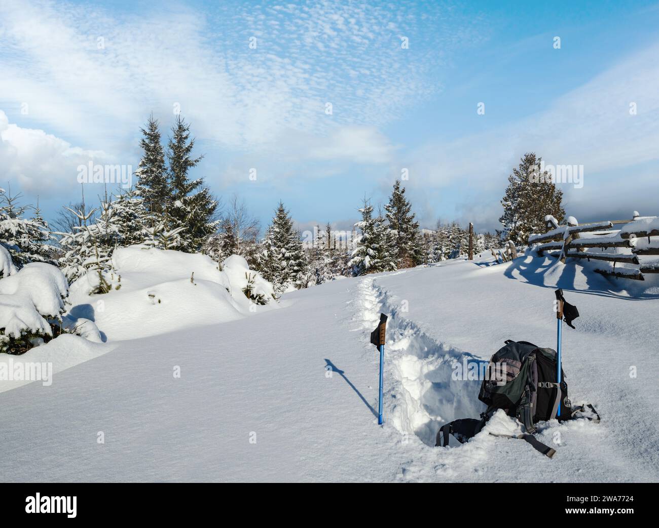 En hiver, en bordure de village alpin isolé, la neige dévie sur le bord de la forêt de sapins de montagne. Sac à dos touristique sur un sentier de randonnée fraîchement trodden. Banque D'Images