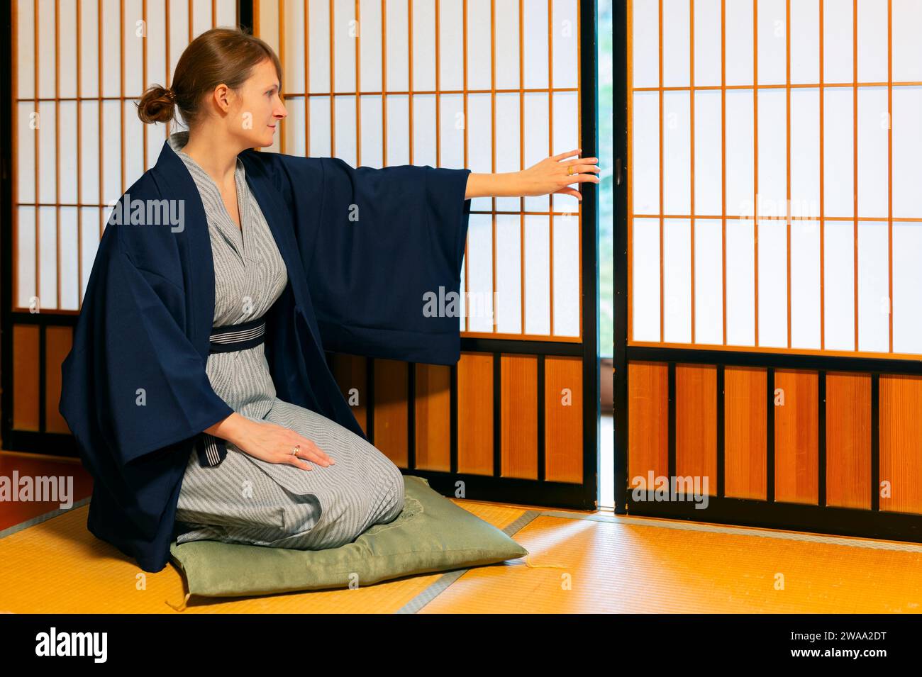Maison traditionnelle japonaise ou ryokan avec gaijin caucasian woman en kimono et chaussettes tabi ouverture coulissante portes papier shoji assis sur tatamis cheminée Banque D'Images