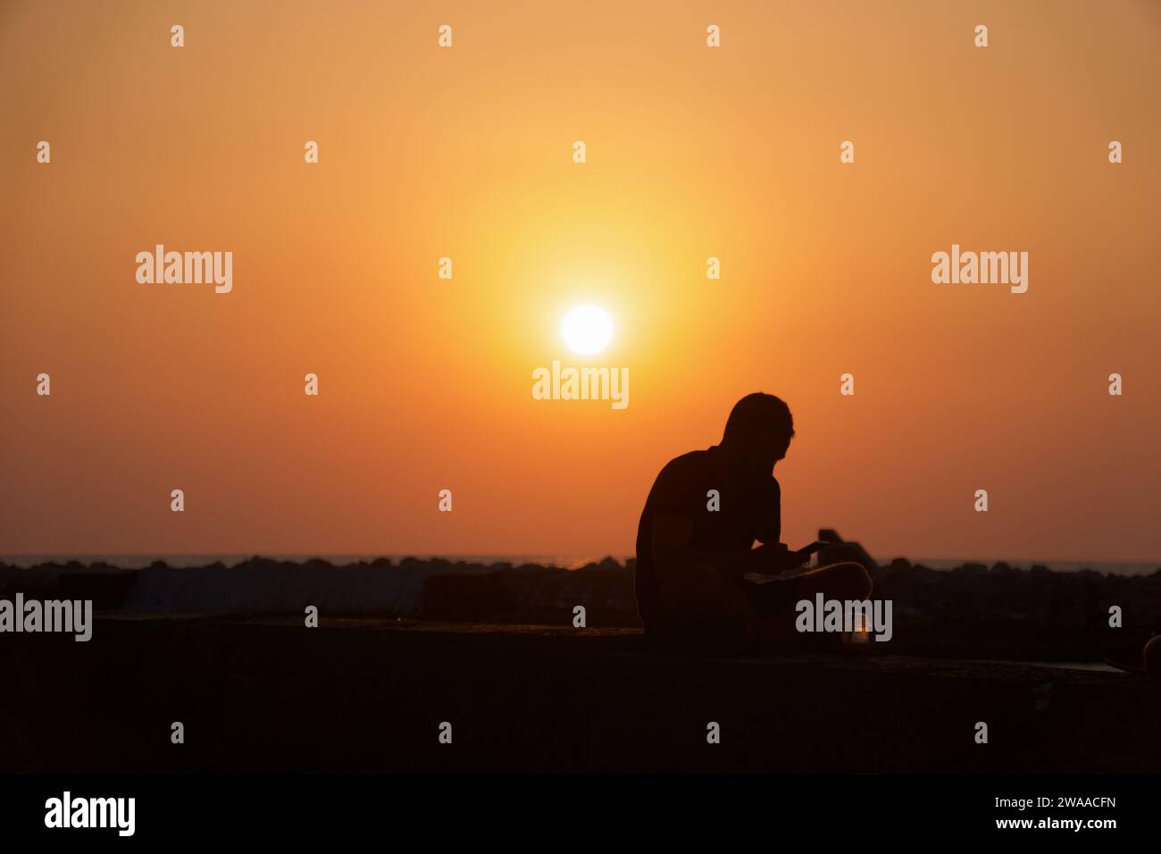 La silhouette d'un homme face au soleil couchant sur la côte de tel-Aviv offre un moment de solitude réfléchie. Banque D'Images