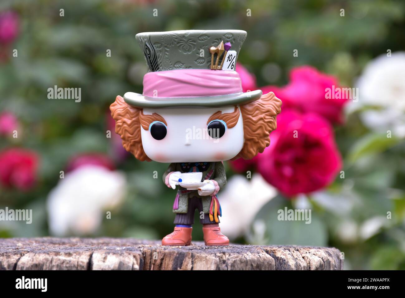 Figurine Funko Pop de Mad Hatter du film fantastique Alice au pays des merveilles de Tim Burton. Roses rouges et blanches, feuilles vertes, jardin, souche en bois. Banque D'Images