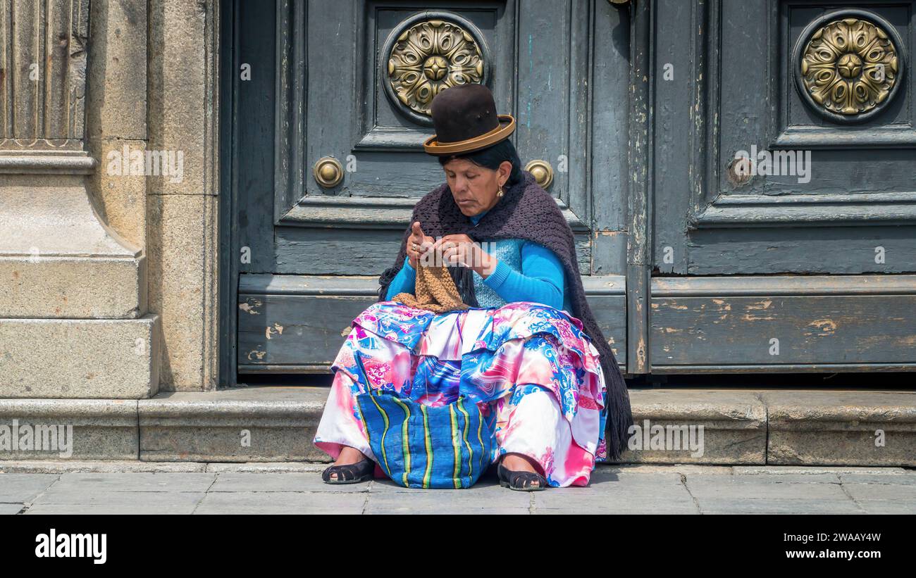 Cusco, Pérou - 24 octobre 2023 : femme péruvienne en vêtements traditionnels tricotant devant une porte près de la rue Banque D'Images
