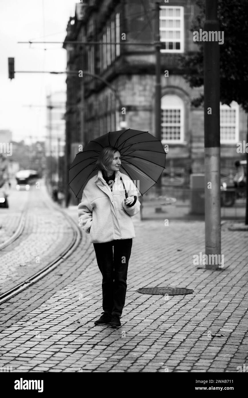 Une femme avec un parapluie marchant dans la rue. Photo noir et blanc. Banque D'Images