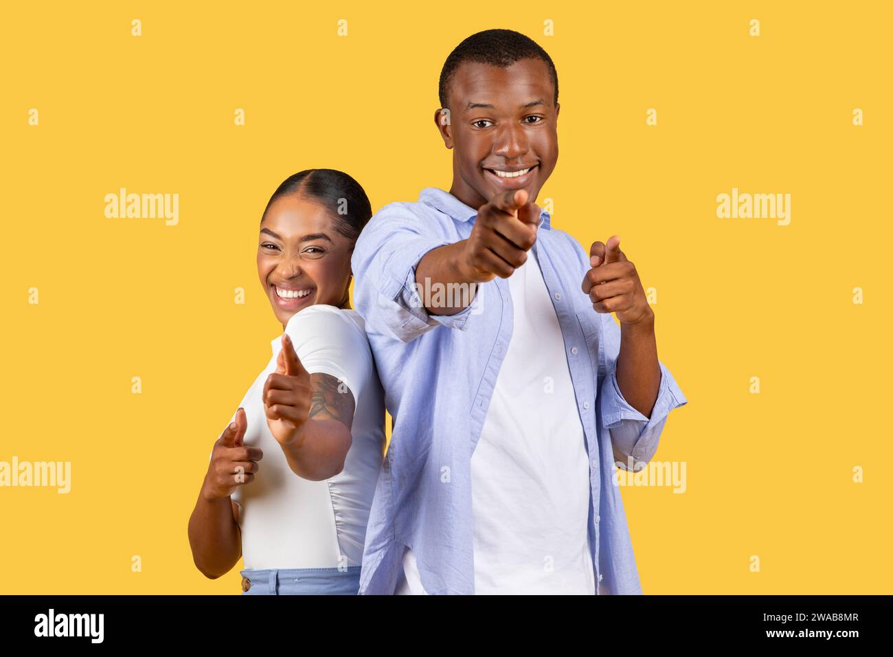 Joyeux couple noir pointant vers le spectateur, sourires engageants, jaune Banque D'Images