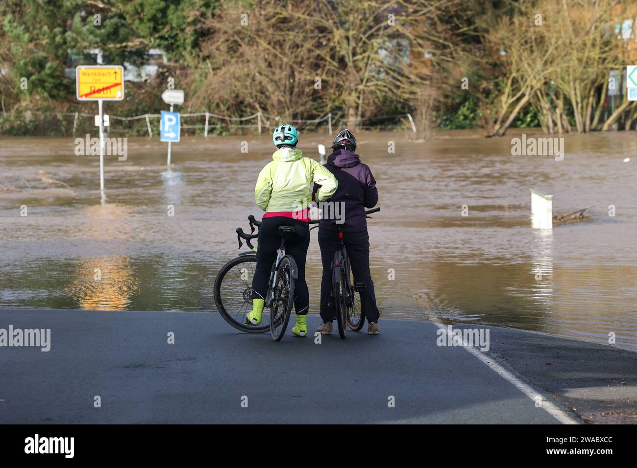 03 janvier 2024, Hesse, Roth (landkreis Marburg-Biedenkopf) : deux cyclistes regardent sur une route inondée. Le Lahn a fait éclater ses berges. La situation des inondations en Hesse est tendue. Photo : Nadine Weigel/DPA/Nadine Weigel/dpa Banque D'Images