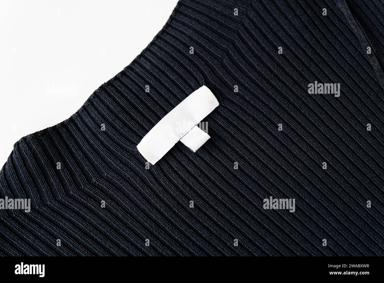 Un vêtement en tissu côtelé noir avec une étiquette blanche de vêtement vierge cousue dessus. L'étiquette est vide, sans texte ni logo Banque D'Images