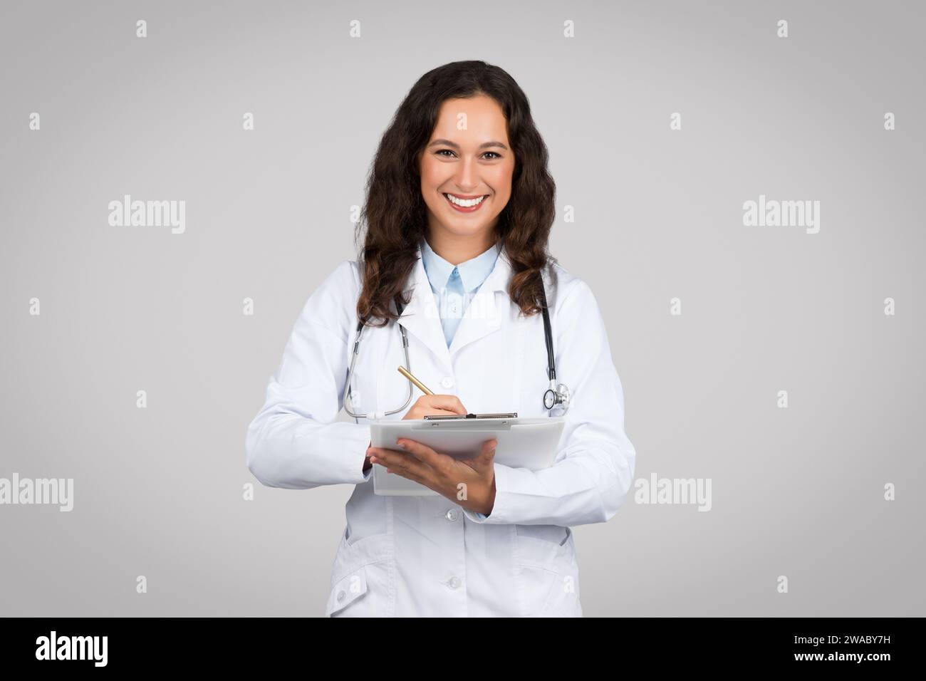 Femme caucasienne médecin heureux en manteau blanc prenant des notes dans le presse-papiers, examen du patient, soins de santé, traitement en clinique Banque D'Images