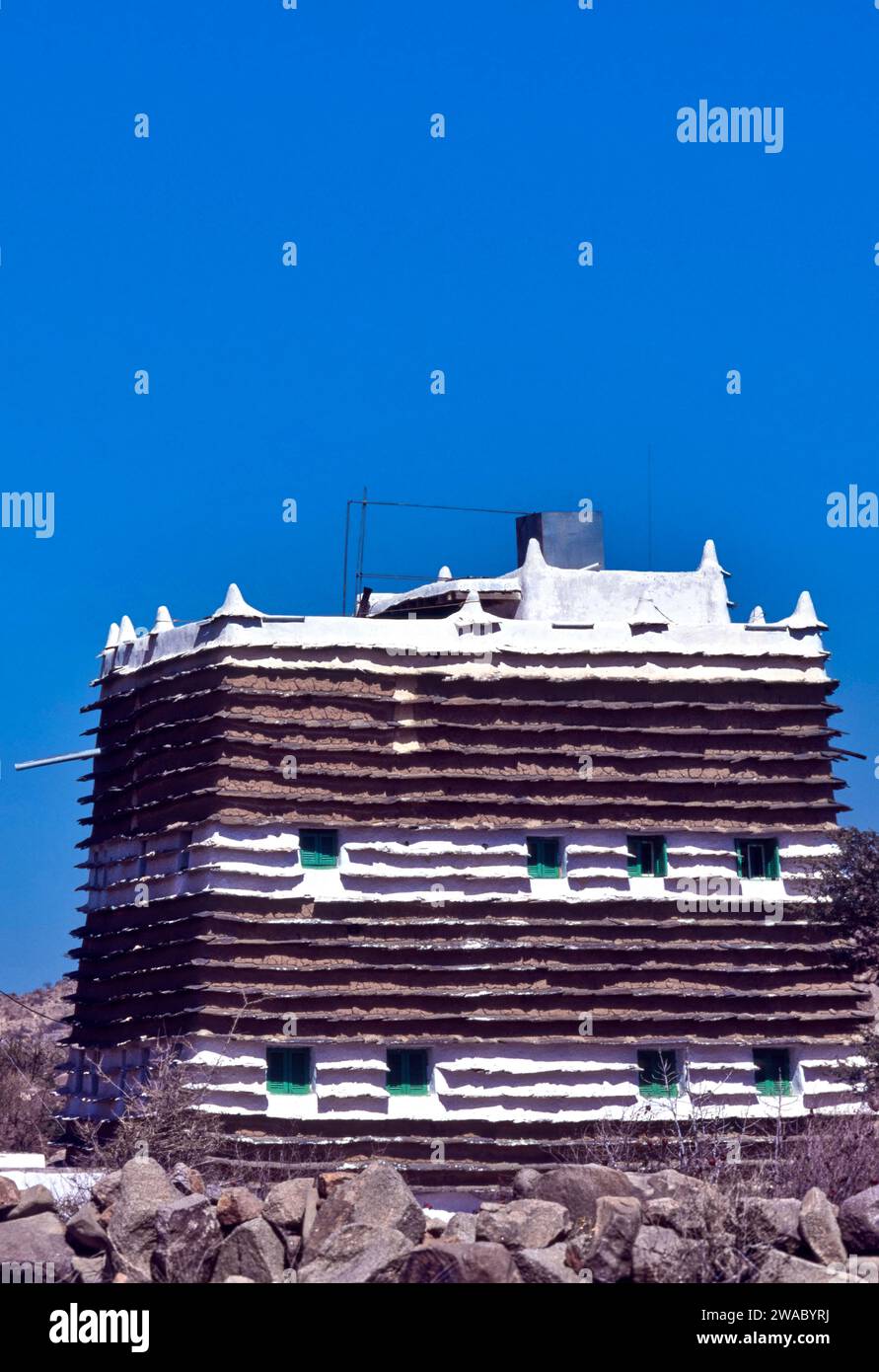 Ciel bleu d'Arabie Saoudite au-dessus d'une vieille maison de village rural muré de boue typique avec de petites fenêtres et des volets verts Banque D'Images