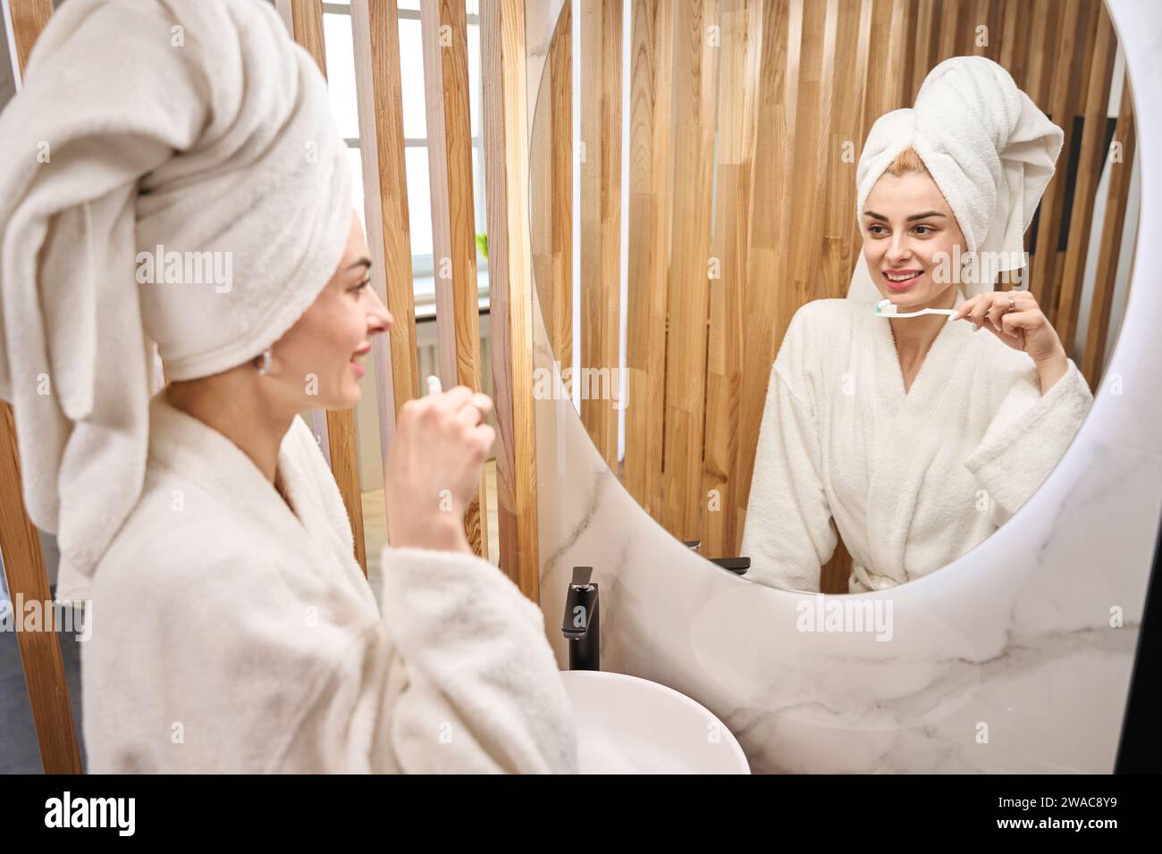 Femme avec une serviette turban se brosse les dents devant le miroir Banque D'Images