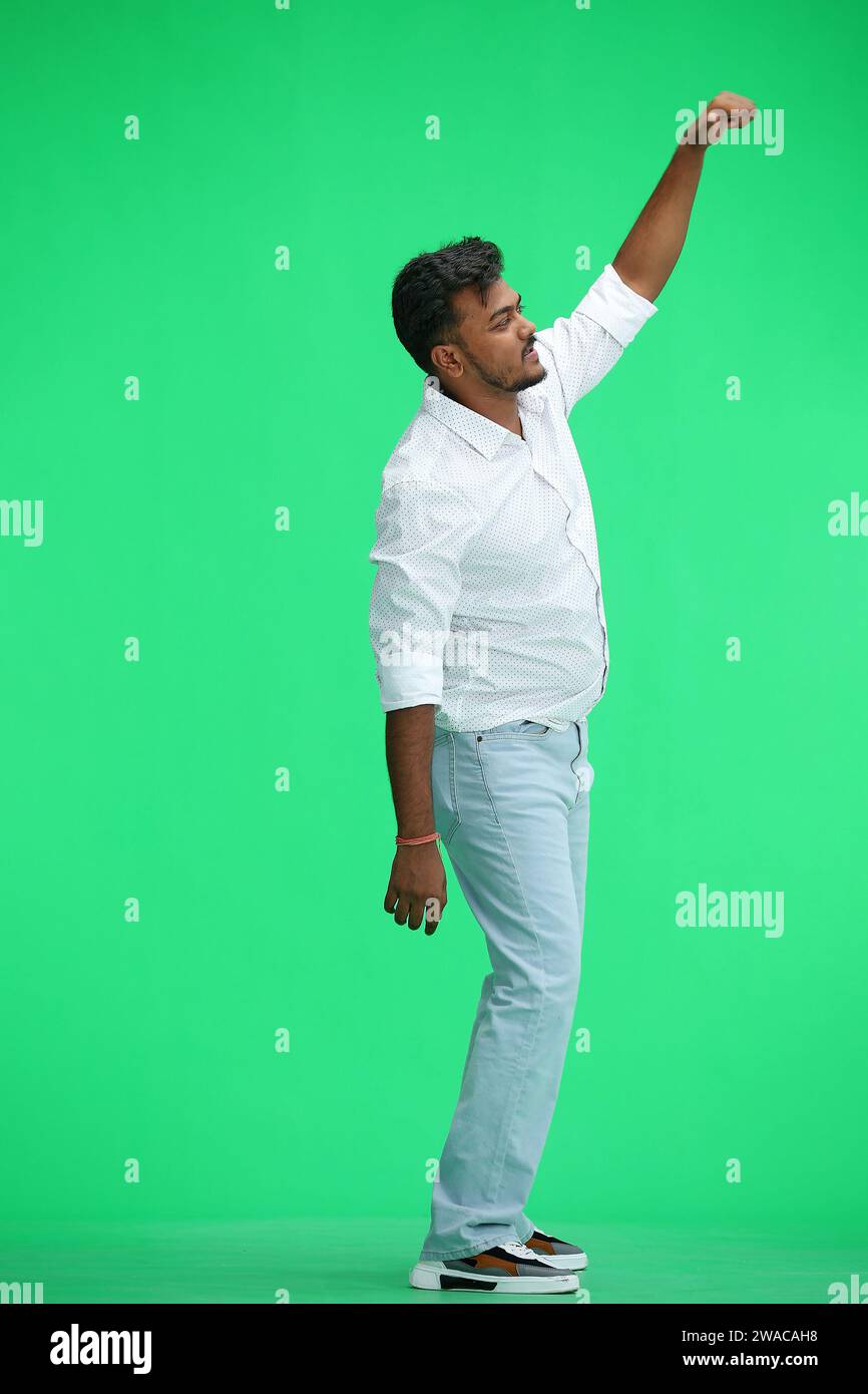 Un homme en chemise blanche, sur fond vert, en pleine hauteur, leva la main, de profil Banque D'Images