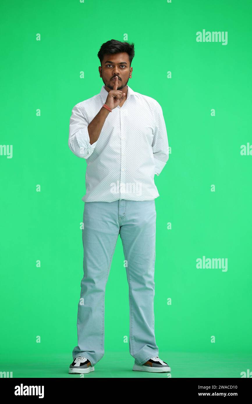 Un homme en chemise blanche, sur fond vert, en pleine hauteur, montre un signe de silence Banque D'Images