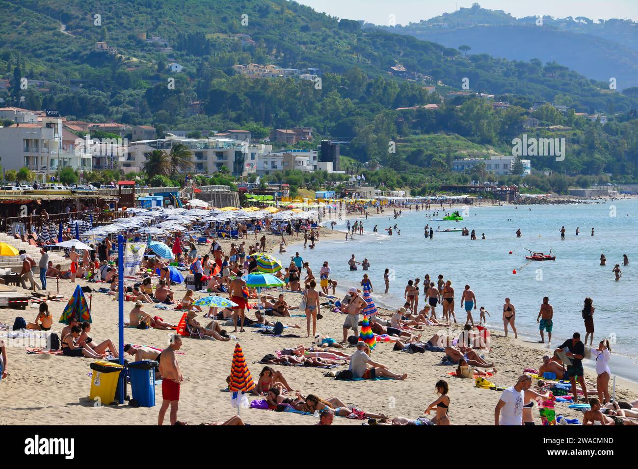 Plage de sable bondée de Cefalù par une journée d'été ensoleillée avec des collines vertes en arrière-plan, Sicile, Italie Banque D'Images