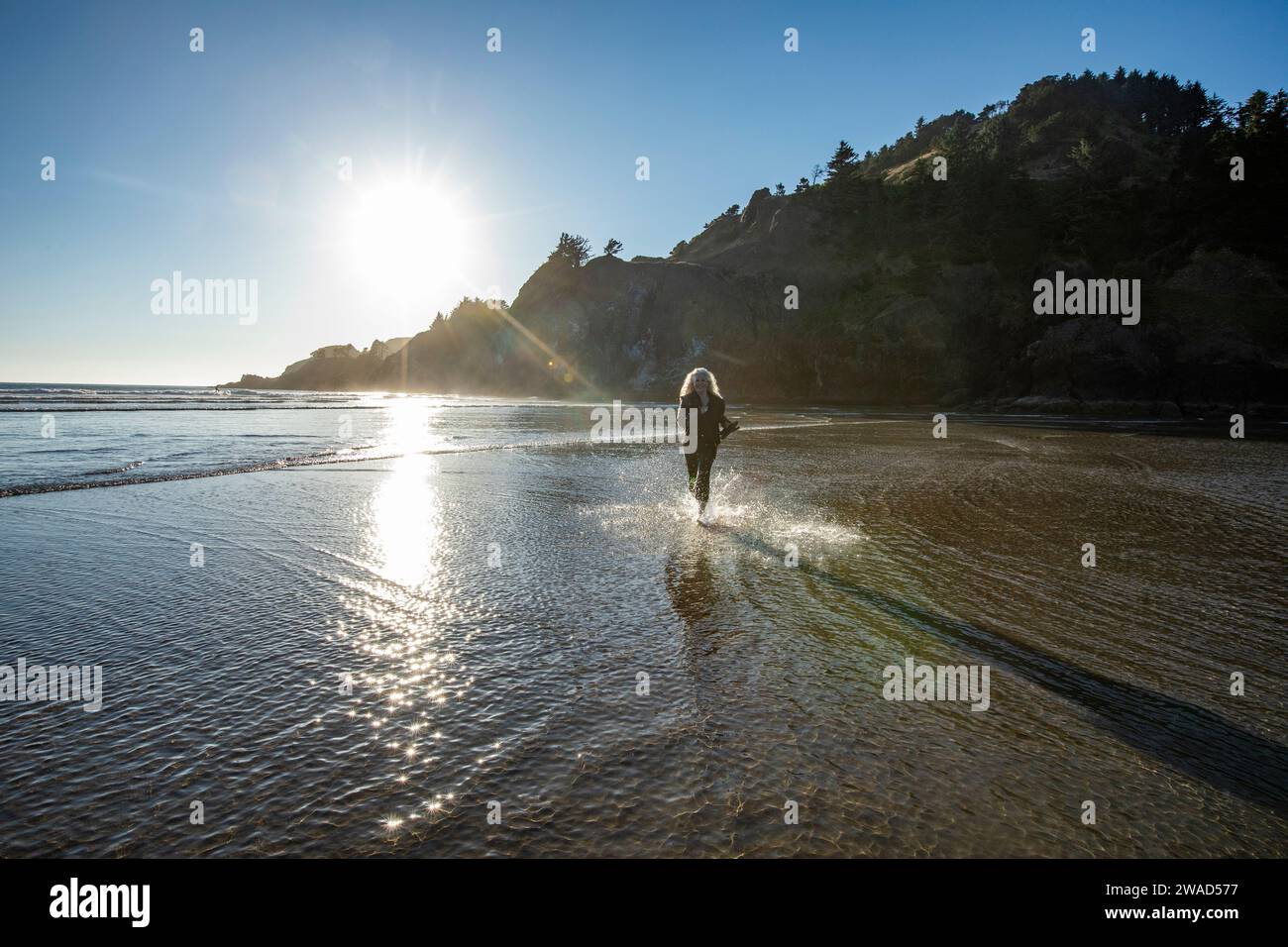 USA, Oregon, Newport, femme courant sur la plage de sable et éclaboussant de l'eau Banque D'Images