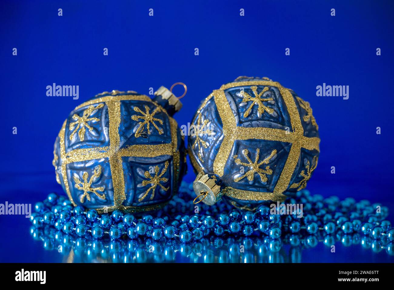 Une paire de boules arbre de Noël bleu et or, photographiées avec un collier de perles bleues, sur un fond bleu Banque D'Images