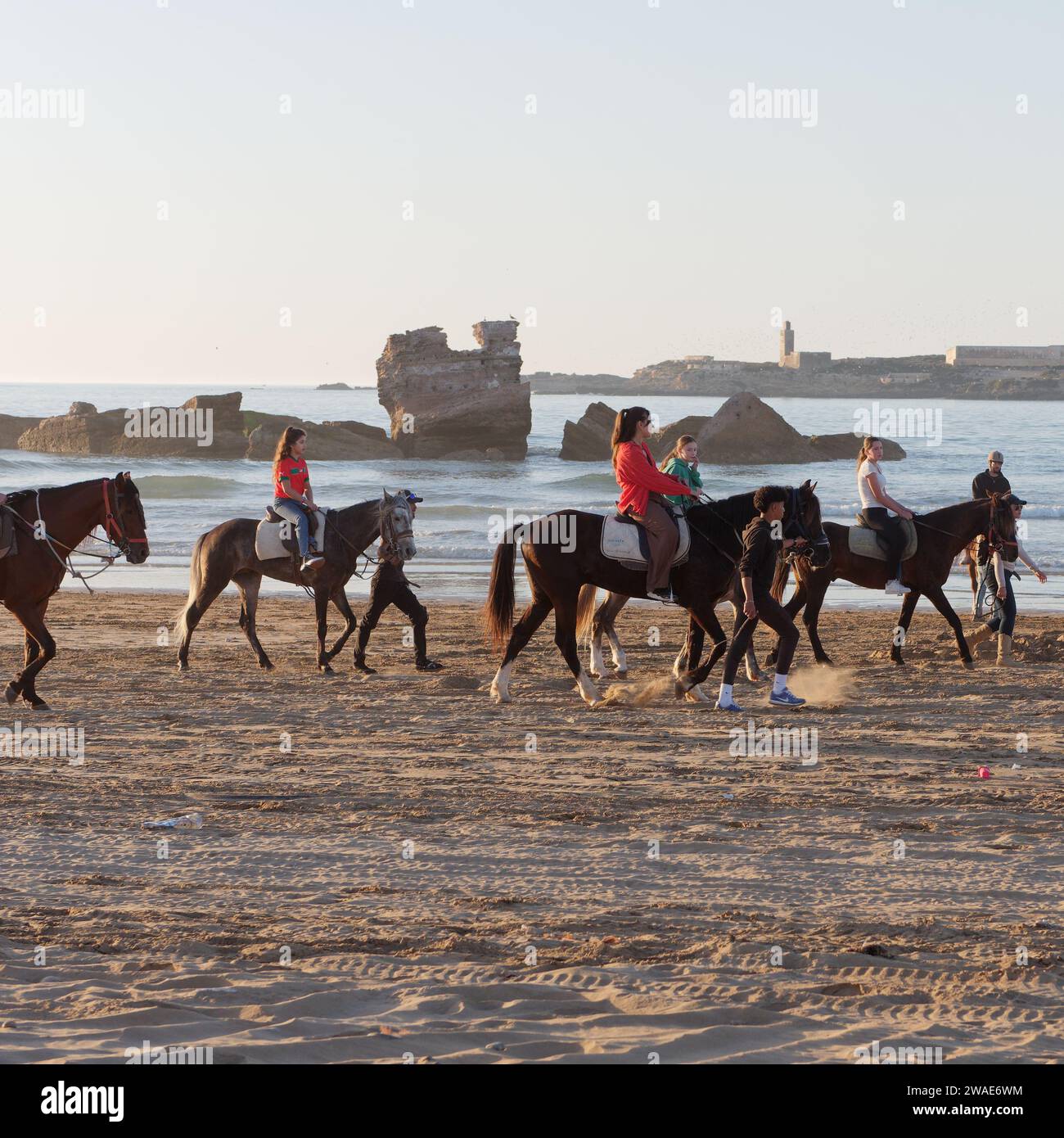 Cavaliers sur une plage avec roche otcrop et île derrière dans la ville d'Essaouira, Maroc, 3 janvier 2024 Banque D'Images