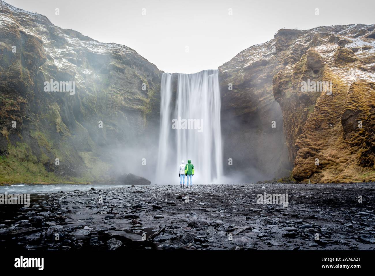 Un homme d'âge moyen se tient en admiration devant une puissante cascade entourée d'une végétation luxuriante Banque D'Images